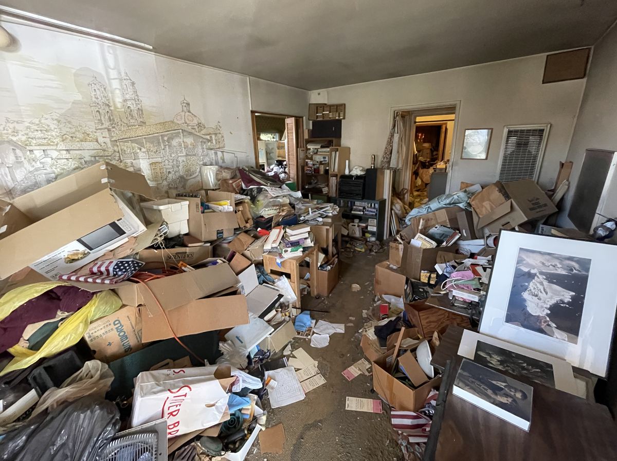 A cluttered room packed floor to ceiling with boxes and belongings before work began